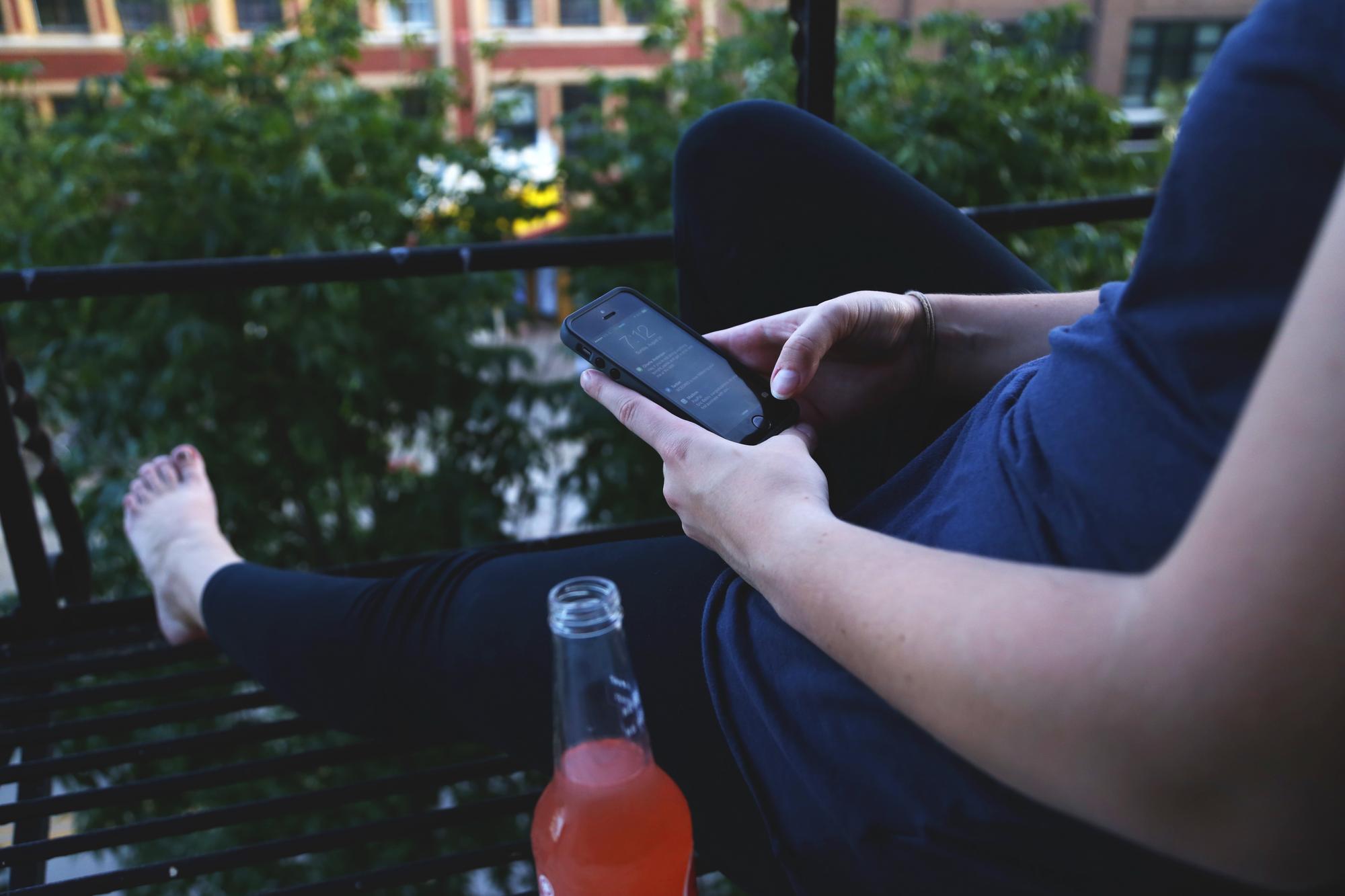 Woman drinking on a balcony looking at her phone'