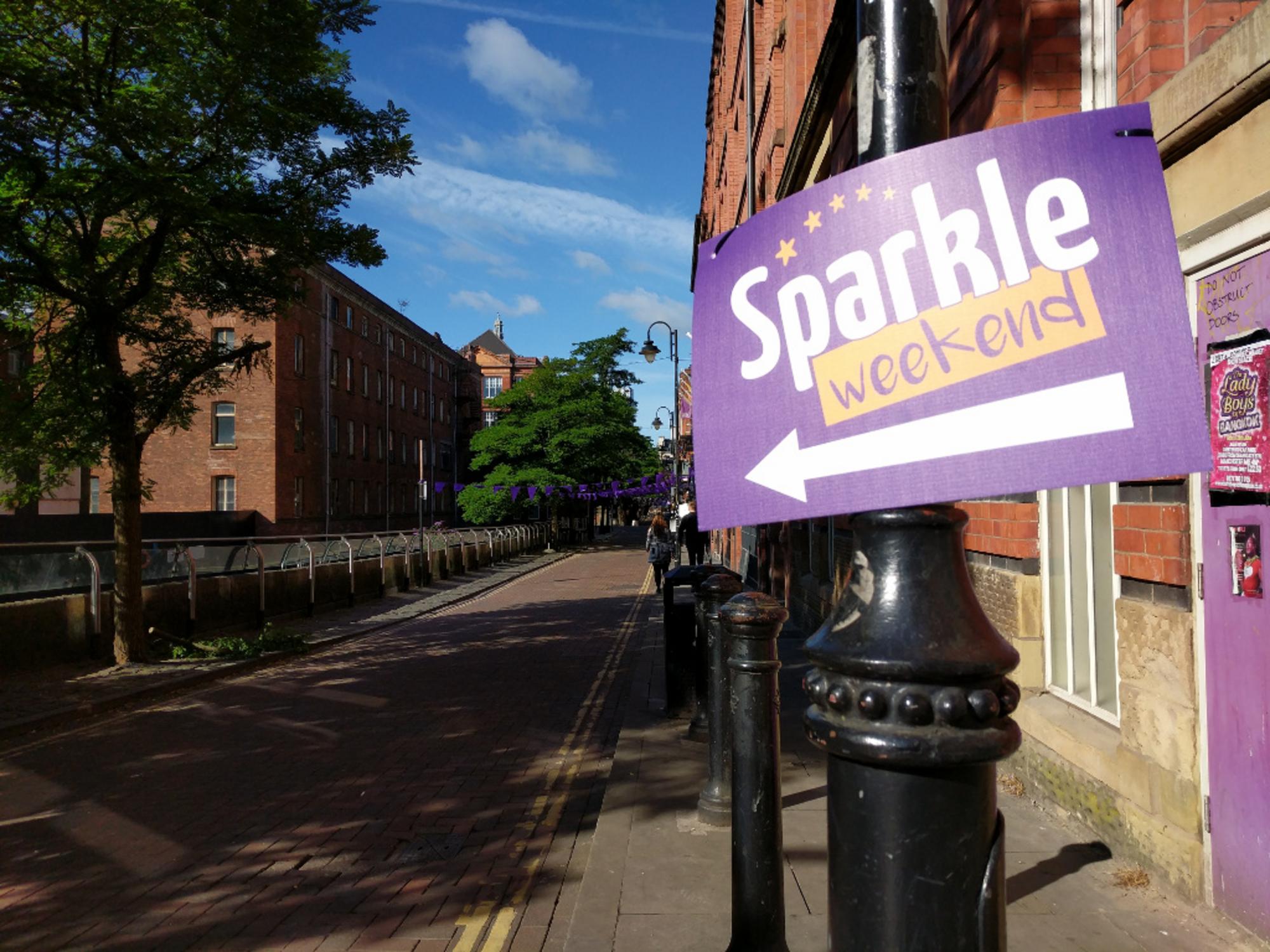 Somewhere near Canal Street, Manchester. A sign attached to a lamppost says "Sparkle Weekend", with an arrow leading the way