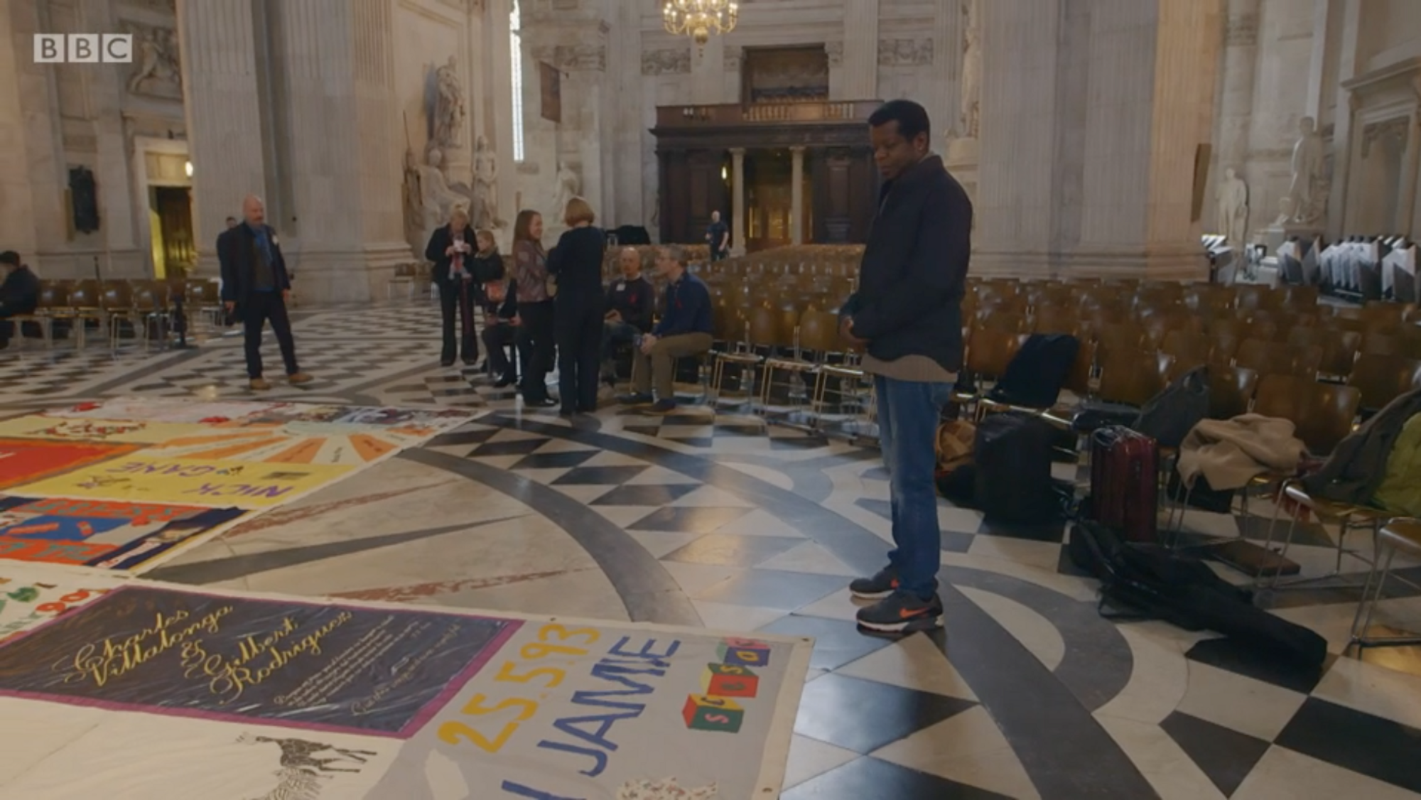 iPlayer screenshot: people respectfully looking at the AIDS tapestry