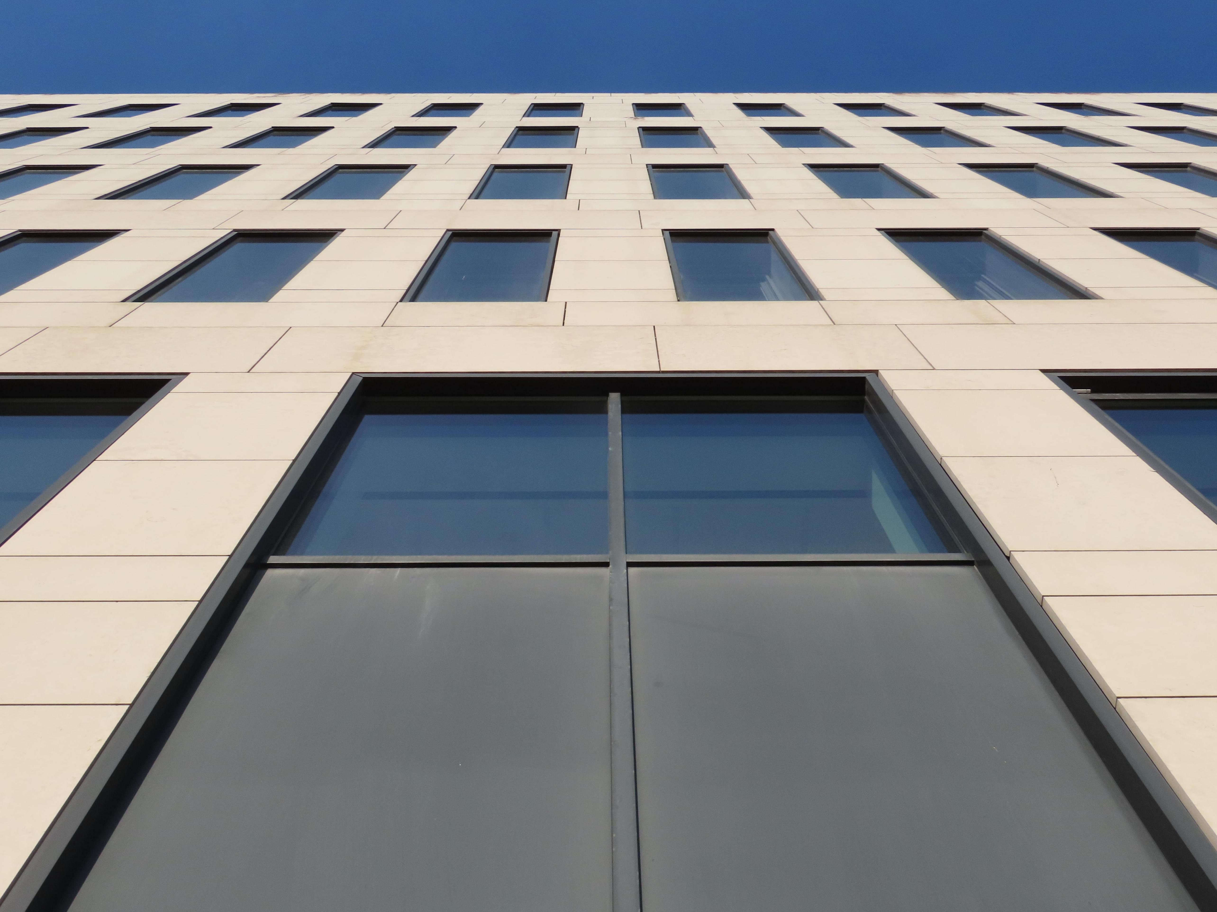 Looking almost directly up, the building fills the bottom 90% of the frame, a bit of clear blue sky above that. The grid of windows almost looks like floor tiles.