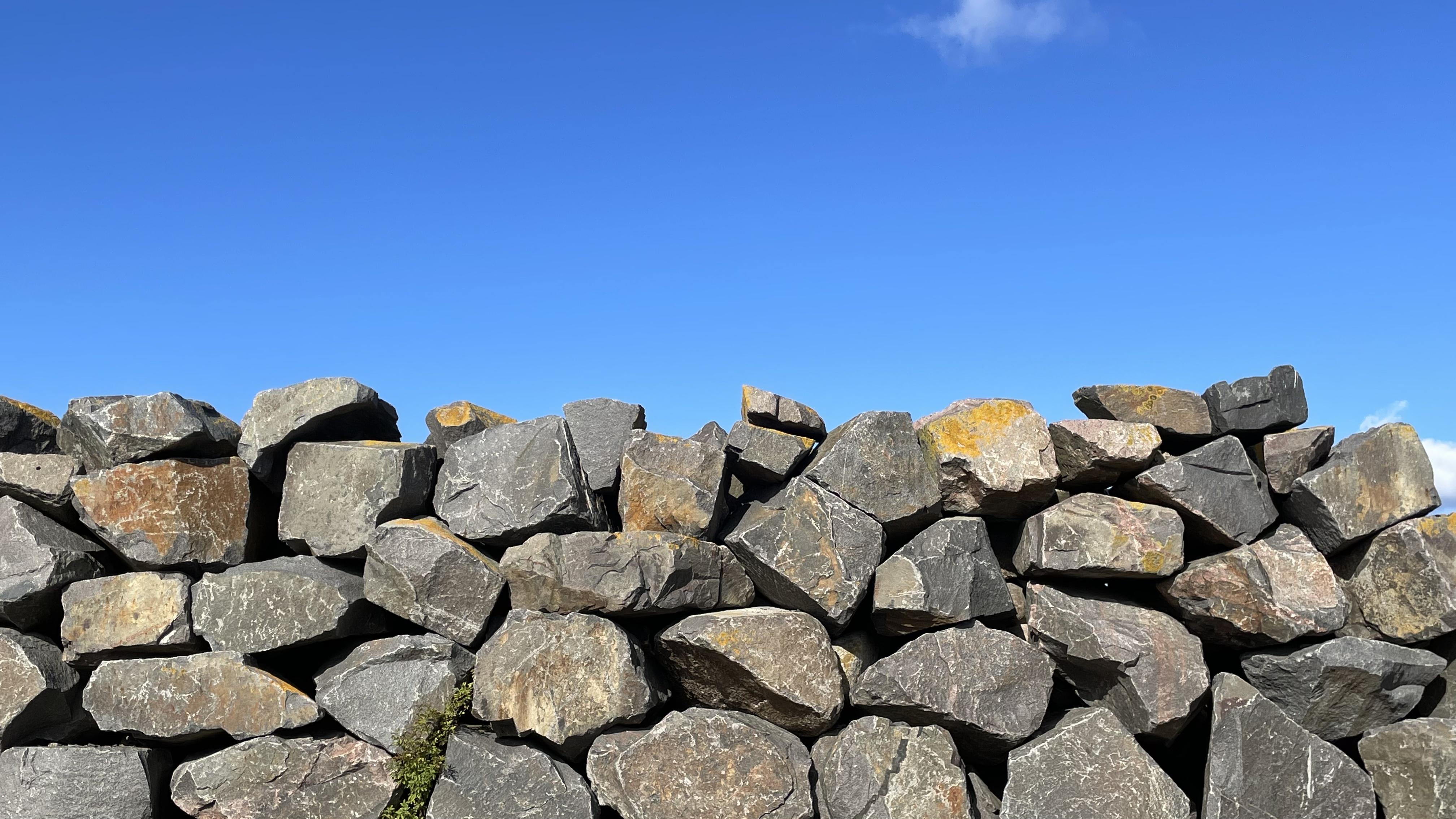 Top half: an almost cloudless bright blue sky. Bottom half: a wall of large granite boulders.